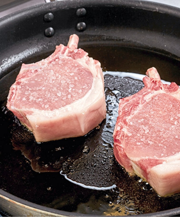 Zwei Schweinskoteletts werden in der Pfanne gesalzen